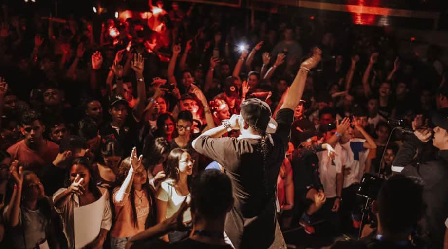 Live performer engaging a tightly packed audience under red club lighting